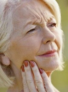 An elderly woman holding her manicured hand to her face, which has a strained expression.