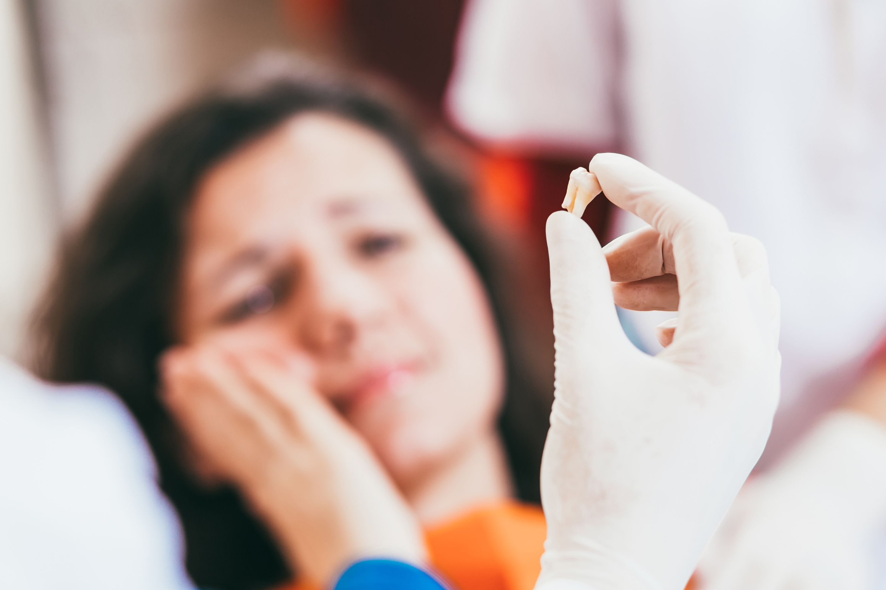 Dentist holding extracted tooth while patient holds jaw in pain